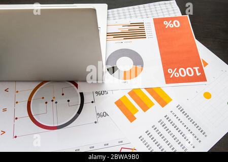 Laptop und Papiere mit Grafiken und Statistiken auf einem dunklen Holztisch Stockfoto