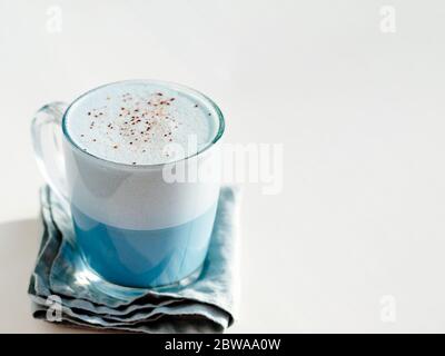 Blaue Erbsenlaatte oder blaue Matcha Latte mit Kopierraum. Heiße frische Milch mit blauen Schmetterlingsblüten oder clitoria ternatea Latte in Glasbecher bei natürlichem Sonnenuntergang hartes Licht. Weißer Hintergrund Stockfoto