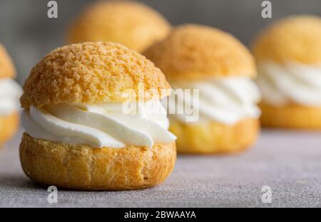 Chou Gebäck Kekse mit Schlagsahne auf grauem Hintergrund gefüllt. Konzept: Bäckerei, französisches Dessert. Selektiver Fokus. Stockfoto