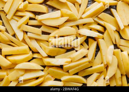 In Scheiben geschnittene Kartoffeln in Gewürzen und Olivenöl werden auf einem Backblech gelegt und fertig gebacken. Gesunde vegane oder vegetarische Zutaten. Flaches Lay Stockfoto