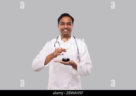 Männlich Arzt zeigt Flasche mit Colorfull Flüssigkeit isoliert. Wissenschaft, Medizin, Virenkonzept. Indischer Mann Arzt Smilling. Stockfoto