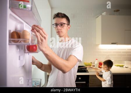 Kamera im Inneren Küche Kühlschrank: Mann öffnet Kühlschranktür, sieht innen. Stockfoto