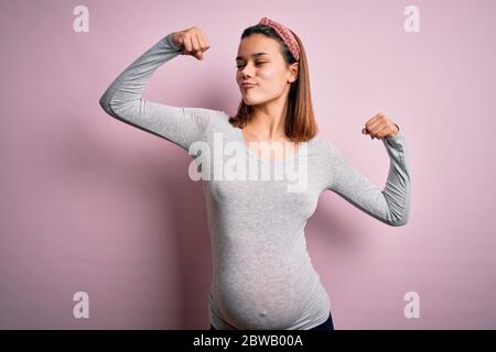 Junge schöne Teenager-Mädchen schwanger erwarten Baby über isoliert rosa Hintergrund zeigt Arme Muskeln lächelnd stolz. Fitnesskonzept. Stockfoto