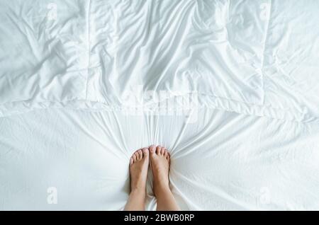 Füße und Zehen treten symmetrisch auf die weißen Falten des Bettes. Stockfoto