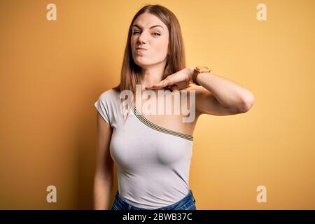 Junge schöne Rotschopf Frau mit lässigem T-Shirt über isolierten gelben Hintergrund Schneiden Kehle mit Hand als Messer, bedrohen Aggression mit furio Stockfoto