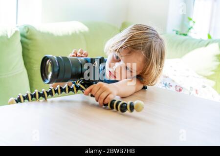 Niedlichen lustigen kleinen Jungen üben in Foto-oder Videoaufnahme mit Kamera auf Stativ. Lifestyle für Jugendliche. Online Influencer, Vlogger Boy, Social Media Konzept. Stockfoto