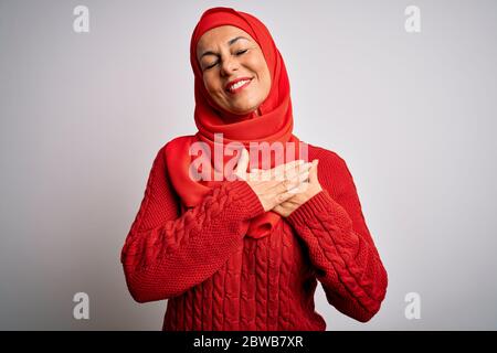Mittelalter Brünette Frau mit muslimischen traditionellen Hijab über isolierten weißen Hintergrund lächelnd mit Händen auf der Brust mit geschlossenen Augen und dankbar ge Stockfoto