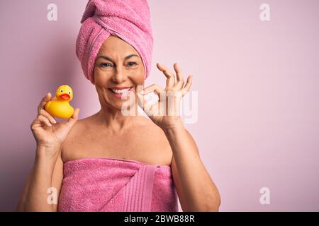 Mittelalter Frau trägt rosa Badetuch von Schönheit Körperpflege halten Gummi gelbe Ente tun ok Zeichen mit Fingern, ausgezeichnetes Symbol Stockfoto