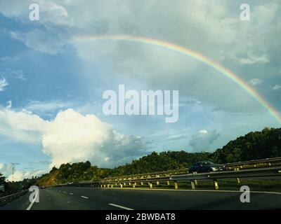 Während der Straße Reisen der Regenbogen erscheinen über die mit klarem Himmel und schöne weiße Wolke schwebt an der Vorderseite. Stockfoto