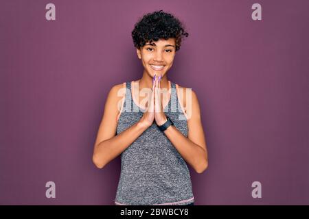 Junge schöne afro amerikanische Sportlerin Ausübung tragen Sportbekleidung mit Händen zusammen beten um Vergebung lächelnd vertrauen zu bitten Stockfoto