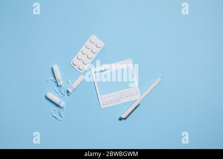 Menstruationshygienische Tampon, Schmerztabletten während der Menstruation auf blauem Hintergrund, femininer Kalender mit Mock Up. Feminine Hygieneprodukte. Draufsicht. Stockfoto