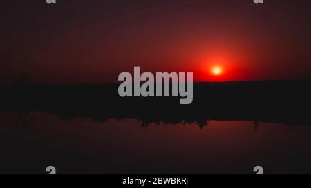 Rote Sonne bei Sonnenuntergang im Fluss reflektiert Stockfoto