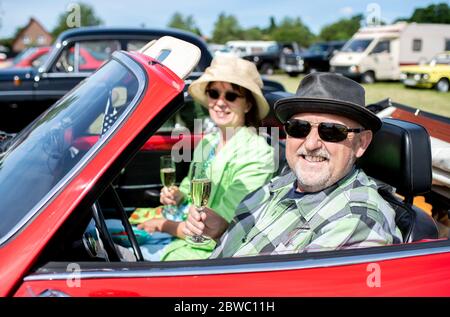 Hude, Deutschland. Mai 2020. Ralf und Traude sitzen mit gefüllten Sektgläsern auf dem Gelände eines Drive-in-Kinos im Wüsting-Bezirk in einem roten Oldtimer. Mehrere hundert Personen in ihren Oldtimern, Youngtimern und amerikanischen Oldtimern nahmen an der Veranstaltung im Oldenburger Kreis Teil. Die Oldtimer-Fans schauten sich den Film "Le Mans 66 - gegen alle Widrigkeiten" in rund 200 historischen Fahrzeugen an. Kredit: Hauke-Christian Dittrich/dpa/Alamy Live News Stockfoto
