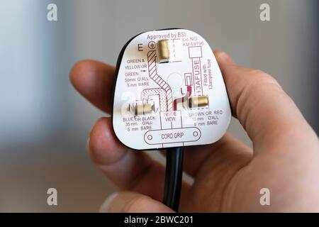 Eine Hand, die einen britischen 3-poligen Standardstecker mit Anweisungen zur Verkabelung der Erdung, des Neutralleiters und der stromführenden Kabel hält Stockfoto