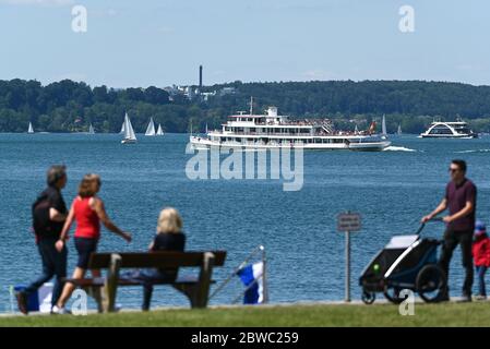 Meersburg, Deutschland. Mai 2020. Ausflügler wandern entlang der Meersburg-Promenade, während im Hintergrund ein Passagierschiff am Bodensee vorbeifährt. Schwimmen im Bodensee ist derzeit generell erlaubt. Die Schwimmbäder bleiben auf unbestimmte Zeit geschlossen, wie die Südwestpresse schreibt. Quelle: Felix Kästle/dpa/Alamy Live News Stockfoto