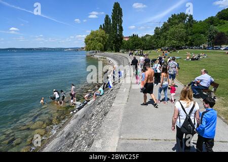 Meersburg, Deutschland. Mai 2020. Ausflügler gehen entlang der Meersburg-Promenade, während eine Frau nach einem Bad gerade aus dem Wasser kommt. Schwimmen im Bodensee ist generell erlaubt. Die Schwimmbäder bleiben auf unbestimmte Zeit geschlossen, wie die Südwestpresse schreibt. Quelle: Felix Kästle/dpa/Alamy Live News Stockfoto