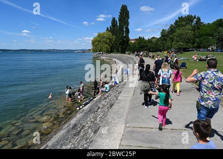 Meersburg, Deutschland. Mai 2020. Ausflügler gehen entlang der Meersburg-Promenade, während eine Frau nach einem Bad gerade aus dem Wasser kommt. Schwimmen im Bodensee ist generell erlaubt. Die Schwimmbäder bleiben auf unbestimmte Zeit geschlossen, wie die Südwestpresse schreibt. Quelle: Felix Kästle/dpa - ACHTUNG: Nur im Vollformat verwenden/dpa/Alamy Live News Stockfoto