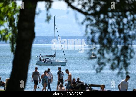 Meersburg, Deutschland. Mai 2020. Ausflügler wandern entlang der Meersburg-Promenade, im Hintergrund fahren mehrere Segelboote vorbei oder segeln auf dem Bodensee. Schwimmen im Bodensee ist derzeit generell erlaubt. Die Schwimmbäder bleiben auf unbestimmte Zeit geschlossen, wie die Südwestpresse schreibt. Quelle: Felix Kästle/dpa/Alamy Live News Stockfoto