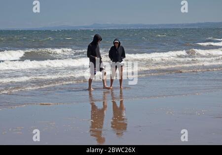 Portobello, Edinburgh, Schottland, Großbritannien. 31 Mai 2020. Sonnig, aber windig mit 14 Grad Celsius und ENE bei 20 km/h und Böen von 38 km/h, viele zogen es vor, eingewickelt zu bleiben, aber diejenigen, die am Strand lagen und saßen, schienen zwischen 12 und 13 Uhr warm genug zu sein. Die beiden Polizisten auf der Promenade könnten sich selbst melden, weil sie ihre soziale Abneigung nicht voneinander gehalten haben. Eine Familie und drei kleine Jungen trotzten dem rauhen Firth of Forth für ein bisschen Spaß im Meer. Quelle: Arch White / Alamy Live News. Stockfoto