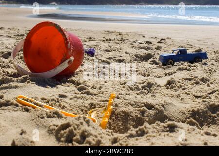Jemand hat sein Spielzeug am Strand vergessen, einen Eimer, einen Plastiksandrechen und einen Polizeiwagen zeigen es. Stockfoto