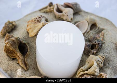 Detail eines Mittelstücks mit maritimem Thema, zusätzlich zu der Kerze in der Mitte und dem Sand um sie herum haben wir mehrere Schneckenschalen. Stockfoto