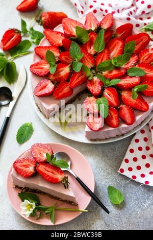 Sommer-Diät Dessert, Käsekuchen ohne Backen. Erdbeerkäsekuchen auf einer Schokoladengranola mit frischen Erdbeeren auf einer hellgrauen Tischplatte. Stockfoto