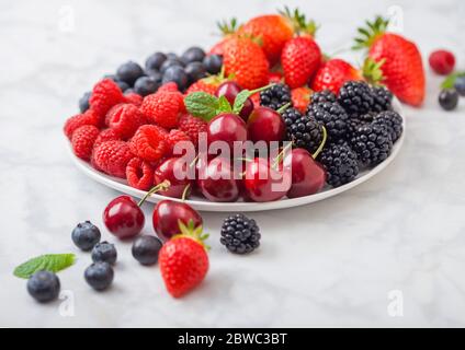 Frische organische Sommer Beeren Mix in weiße Platte auf Marmor Hintergrund. Himbeeren, Erdbeeren, Heidelbeeren, Brombeeren und Kirschen. Ansicht von oben Stockfoto