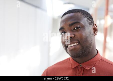 Kopf- und Schulterporträt des zeitgenössischen afroamerikanischen Mannes, der vor weißem Hintergrund in der Kamera posiert und lächelt, während er im Büro posiert Stockfoto