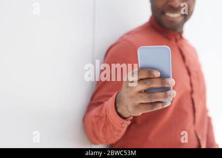 Nahaufnahme eines nicht erkennbaren afroamerikanischen Mannes mit Smartphone, während sie gegen die Wand stehen und lächeln, konzentrieren sich auf die männliche Hand, die das Telefon in fo hält Stockfoto