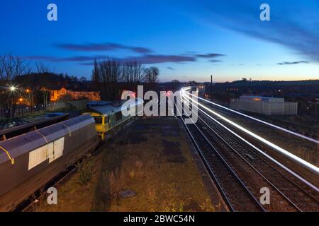 Vorbei an Zügen in Barnetby, vor Sonnenaufgang. Freightliner der Klasse 66 wartet mit einem Kohlezug, während die leichten Trails eines anderen Zuges vorbeiziehen Stockfoto