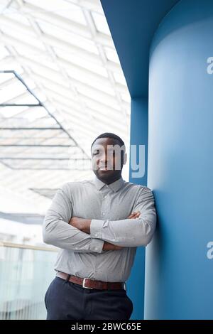 Vertikale Taille oben Porträt des erfolgreichen afroamerikanischen Geschäftsmann Blick auf die Kamera, während gegen die Wand in modernen Bürogebäude, Kopie Spa gelehnt Stockfoto