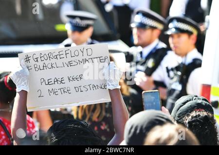 Ein Demonstrator hält ein Schild hoch, das die Menschen an soziale Distanz während eines Black Lives Matter Protests vor der US-Botschaft in London erinnert. Der Protest folgt dem Tod von George Floyd in Minneapolis, US, diese Woche, die einen Polizeibeamten gesehen hat, der mit Mord dritten Grades aufgeladen wird. Stockfoto