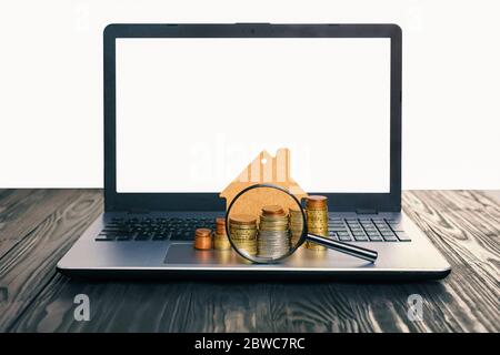 Konzept des Verkaufs und der Vermietung von Wohnungen, Hypotheken, Darlehen. Laptop mit leerem Bildschirm und Haufen von Euro-Münzen, Mock-up eines Hauses. Stockfoto