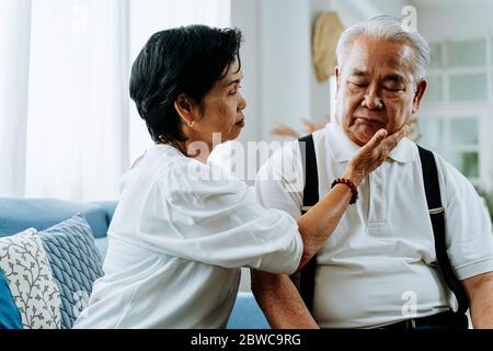 Unglücklich im Ruhestand asiatische ältere Paar sitzt auf dem Sofa, während ältere Frau tröstlich ihren traurigen Mann zu Hause Stockfoto