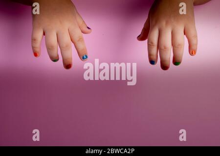 Die Hände des kleinen Mädchens in verschiedenen Farben bemalte Nägel. Modekonzept Stockfoto