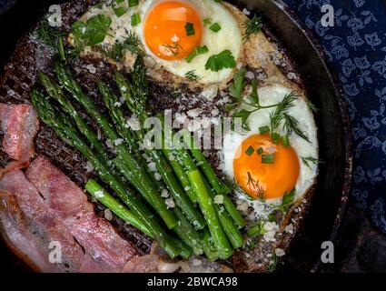 Köstliches Frühstück Mittagessen Zweig der Spiegeleier, Speck, grünen Spargel, Grün und Parmesan-Käse auf Pfanne. Draufsicht, Kopie Raum Stockfoto