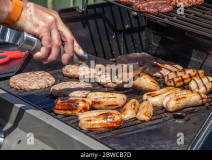 Ein Barbecue-Grill mit Burger und Würstchen wird an einem sonnigen Tag betreut. Stockfoto