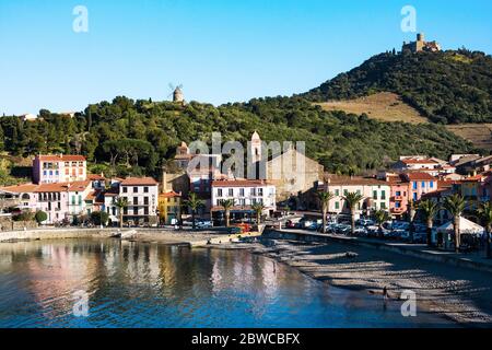 Collioure, Frankreich - Februar 24, 2020: Strandhotels in Collioure Dorf mit Windmühle auf dem Hügel, Roussillon, Vermilion Küste, Pyrenäen Orientales, Franc Stockfoto