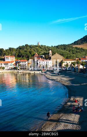 Collioure, Frankreich - Februar 24, 2020: Strandhotels in Collioure Dorf mit Windmühle auf dem Hügel, Roussillon, Vermilion Küste, Pyrenäen Orientales, Franc Stockfoto