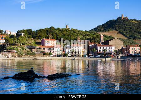 Collioure, Frankreich - Februar 24, 2020: Strandhotels in Collioure Dorf mit Windmühle auf dem Hügel, Roussillon, Vermilion Küste, Pyrenäen Orientales, Franc Stockfoto