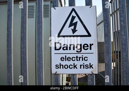 Rechteckiges schwarz-weißes Schild - Gefahr Stromschlag Risiko - mit Warndreieck mit Strom Blitzsymbol, auf Metallzaun an Umspannwerk Stockfoto