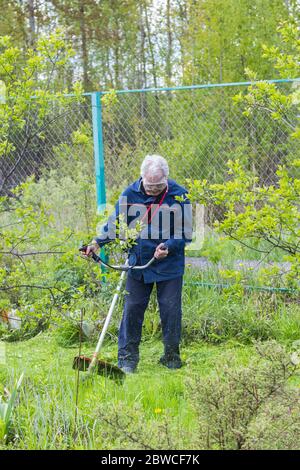 Ein Arbeiter mäht Gras und Unkraut mit einem Rasenmäher auf dem Land Stockfoto