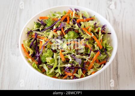 Hausgemachte Raw zerfetzte Broccoli Slaw in einer weißen Schüssel auf weißem Holzhintergrund, Seitenansicht. Stockfoto