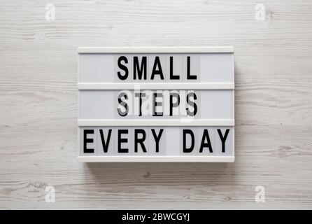 „kleine Schritte jeden Tag“-Worte auf einem Leuchtkasten auf weißem Holzhintergrund, Draufsicht. Über Kopf, von oben, flach gelegt. Stockfoto