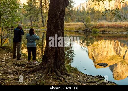 Ein Paar fotografiert die Spiegelung der Landschaft im Wasser des Merced River im Yosemite National Park Stockfoto