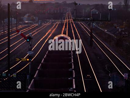 Güterzug mit Eisenerz, der die mechanischen Semaphore-Signale bei Barnetby passiert, während die untergehende Sonne von den Schienen scheint Stockfoto