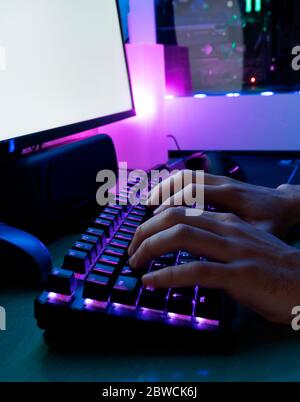 Bild von den Händen des Mannes, der tippt. Hände eines Spielers auf einer Tastatur. Hintergrund wird mit LED-Leuchten beleuchtet. Stockfoto