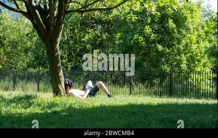 Glasgow, Schottland, Großbritannien. Mai 2020. Ein Mann, der an einem warmen und sonnigen Sonntagnachmittag auf dem Gras an einem Baum in Glasgow Green liegt. Die schottische Regierung kündigte am 28. Mai eine Lockerung der Sperrregeln für das Coronavirus an. Kredit: Skully/Alamy Live News Stockfoto