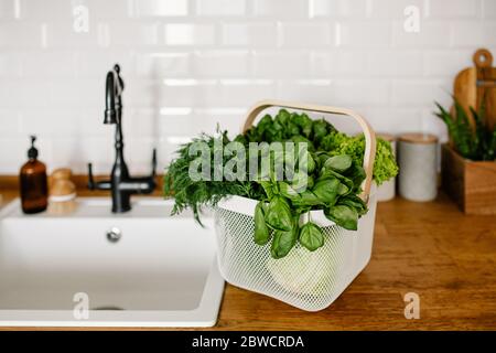 Frische Salate und Kräuter in Metallkorb auf dem Tisch in der Küche. Zero Waste Shopping Konzept. Nachhaltiges Leben Stockfoto