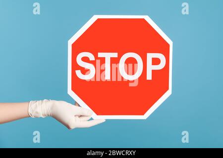 Profil Seitenansicht Nahaufnahme der menschlichen Hand in weißen chirurgischen Handschuhen halten und zeigen Stop-Zeichen. Indoor, Studio-Aufnahme, isoliert auf blauem Hintergrund. Stockfoto